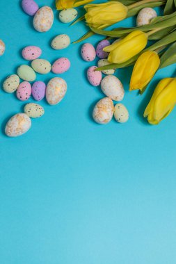 Yellow tulip flowers and easter eggs on blue background. Top view with copy space. Happy easter greeting card. High quality photo