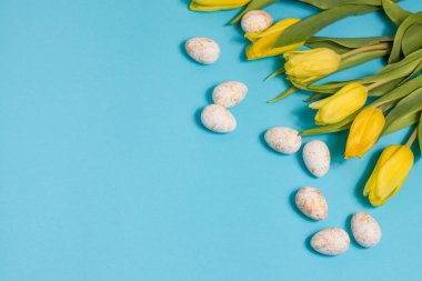Yellow tulip flowers and easter eggs on blue background. Top view with copy space. Happy easter greeting card. High quality photo