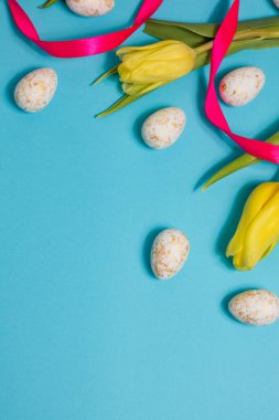 Yellow tulip flowers and easter eggs on blue background. Top view with copy space. Happy easter greeting card. High quality photo