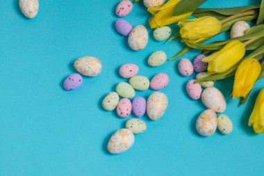 Yellow tulip flowers and easter eggs on blue background. Top view with copy space. Happy easter greeting card. High quality photo