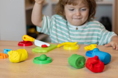 Evde oynayan sevimli küçük bir çocuk, çok renkli plastik kalıplar çıkarıyor. Kil kaplamalı bebek heykelleri. Hamur oyna