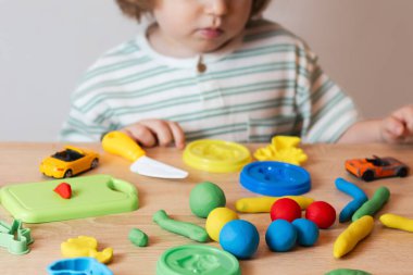 Evde oynayan sevimli küçük bir çocuk, çok renkli plastik kalıplar çıkarıyor. Kil kaplamalı bebek heykelleri. Hamur oyna