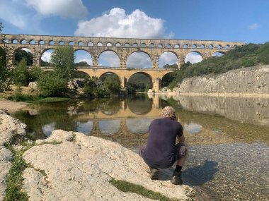 Antik Roma Pont du Gard su kemeri ve viyadük köprüsünün yanında oturan adam, Güney Fransa 'da Nimes yakınlarındaki antik Roma köprülerinin en yükseği..