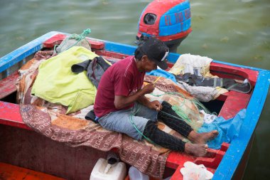 Balıkçı teknede otururken ağlar hazırlar. 