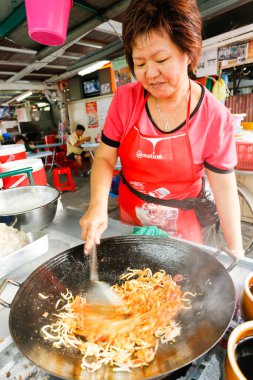 Georgetown, Penang, Malezya - 22 Temmuz 2014: Malezyalı Çinli kadın, Malezya usulü kızarmış erişte pişiriyor (Char Koay Teow). 