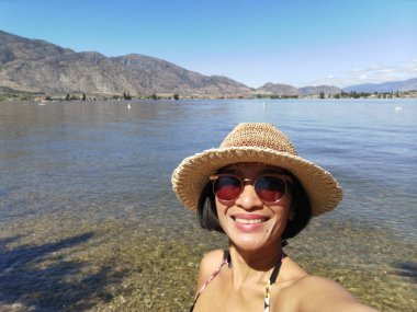 Okanagan Vadisi 'ndeki Osoyoos Gölü' ne bakan Haynes Point eyalet parkından selfie çeken kadın turist..