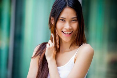 Genç ve güzel Taylandlı bir kadının portresi. Uzun saçlı, kameraya bakan ve yüzünde neşeli bir ifadeyle gülümseyen..