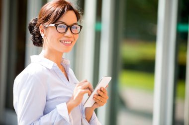 Malezyalı gülümseyen, göz kapağı takan ve akıllı telefon üzerinde çalışan yetişkin bir kadının portresi. İş kavramı kendinden emin ve başarılı iş kadını.