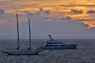 Tayland 'ın Phuket Adası yakınlarında günbatımında yat ve motorlu tekne kullanan lüks bir yelkenli..