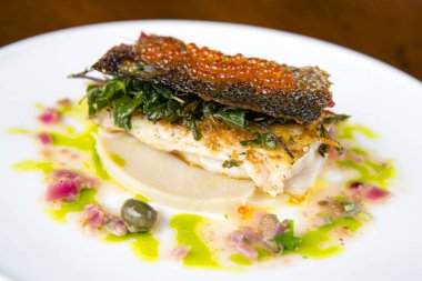 Kurutulmuş somon aperatifi, çıtır balık derisi, somon yumurtalarıyla kaplı, deniz tarağı köpüğü yatağında..