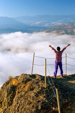 Dev Başlı Dağ 'ın zirvesinde kolları açık bir turist aşağıdaki vadi ve gölü kaplayan sis manzaralı Summerland, British Columbia, Kanada' daki Okanagan Vadisi 'nde.