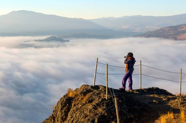 Summerland, British Columbia, Kanada 'daki vadiyi ve gölü kaplayan sise bakan Giant' s Head Dağı 'nın zirvesinden tek başına fotoğraf çeken bir kadın..