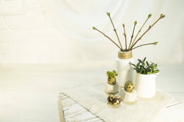 Branches in buds and young leaves in a vase in the interior. Composition of quail egg and green moss on a stand. The idea of festive decoration of the room for Easter. High quality photo