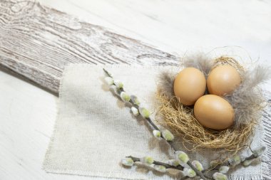 Three orange eggs lie in a nest on a table, on wooden boards. Easter card for the holiday. High quality photo
