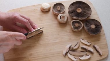 Bir adam Agaricus mantarlarını dilimlere ayırıyor. Masanın üzerinde taze, büyük ve küçük mantar kapakları var. Yüksek kalite 4k görüntü