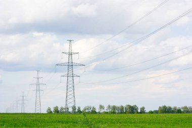Güç direkleri, beyaz bulutlu mavi gökyüzüne karşı yeşil bir alan arasında yer alıyor. Yüksek kalite fotoğraf