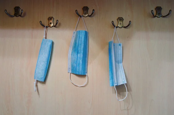 Close-up view of coat rack with three medical masks are hanging on wooden wall. Antivirus (Coronavirus, COVID-19) advertising concept. The new normal combines clothing and accessories.