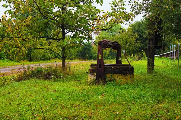 Close-up view of abandoned old well in typical Ukrainian village.  Ancient draw-well surrounded by autumn colored trees. Rural landscape view of typical Ukrainian village at autumn rainy day.
