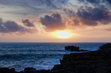 Scenic landscape view of dramatic sunset sky at rocky shore of the Atlantic ocean near Cascais, Portugal.