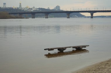 2023 ilkbaharında Kyiv 'deki yüksek su manzarası. Suda eski ahşap bir bank. Dnipro Nehri 'nin sol kıyısındaki Berezniaky mahallesinde halk plajı. Arka planda bulanık şehir manzarası.