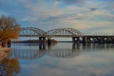 Gün batımında Kyiv 'deki Dnipro Nehri manzarası. Köprü, Dinyeper Nehri 'nin sakin suyuna yansıdı. Arka planda beyaz bulutlar olan mavi gökyüzü. Doğa konsepti.