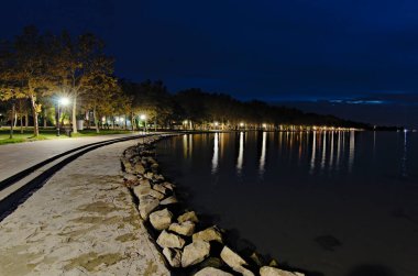 Balaton Gölü ve ünlü Uçak Ağaçları Geçidi 'nin gece ışığı manzarası. Ünlü turistik yer ve romantik seyahat yeri. Manzara ve doğa kavramı. Balatonfold, Macaristan.