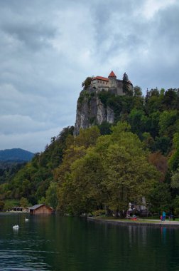 Bled Gölü ile bir dağın tepesindeki Bled Kalesi 'nin resimli manzarası. Slovenya 'nın en ünlü gölü. Ünlü turistik yer ve romantik seyahat yeri. Bulutlu hava.