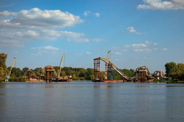 Panoramik manzara, nehir üzerinde yeni bir yaya köprüsü inşa etmek için çelik yapıların monte edilmesi sürecine bakıyor. Köprü inşa ediliyor. Ukrayna, Kyiv 'deki Obolon mahallesi.