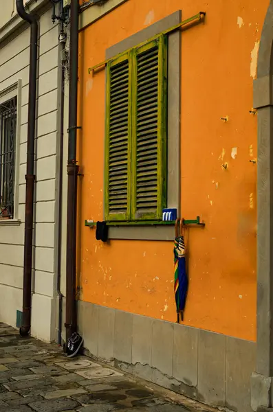 Vintage orange wall with window closed by green wooden shutters. Wall with rough surface. Wooden shutters on the window of a traditional house in Pisa. Typical architecture of Tuscany region, Italy.