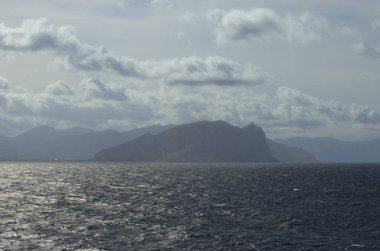 Işık sisi içinde ufukta dağların siluetleri olan manzaralı deniz manzarası. Deniz ve karanın soyut görüntüsü. Seyahat ve turizm kavramı.