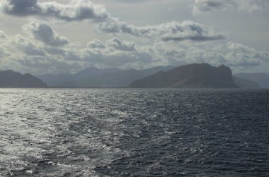 Işık sisi içinde ufukta dağların siluetleri olan manzaralı deniz manzarası. Deniz ve karanın soyut görüntüsü. Sicilya adası, İtalya. Seyahat ve turizm kavramı.