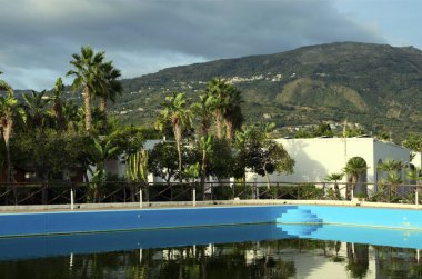 Büyük yüzme havuzunun manzarası ve arka planda palmiye ağaçları. Marina di Patti, İtalya 'nın Sicilya eyaletinde yer alan bir şehirdir. Seyahat ve turizm kavramı.