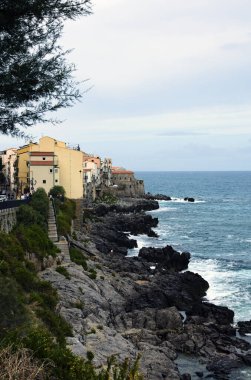 Kayalıklardaki renkli evlerin etkileyici manzarası. Dalgalar kayaları vuruyor, sonbahar mevsiminde Tyrhenian denizi. Sicilya 'nın eski Cefalu kasabası. Doğa bileşimi. Seyahat ve turizm kavramı.