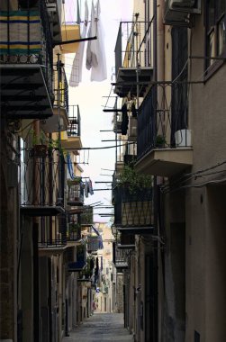 Eski evlerin arasında merdivenleri olan tipik dar kaldırım taşı caddesi. İç çamaşırları balkon çitinde kuruyor. Ortaçağ Cefalu 'sunda geleneksel cadde. Cefalu, Sicilya, İtalya.