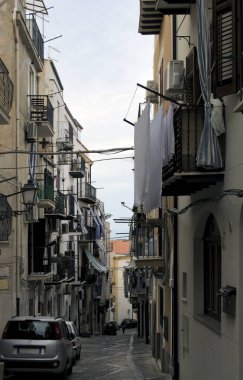 Eski konutlar arasındaki otantik dar kaldırım taşı caddesi. Ortaçağ Cefalu 'sunda geleneksel cadde. İç çamaşırları balkon çitinde kuruyor. Seyahat ve turizm kavramı.