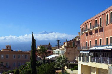 Taormina, İtalya-29 Ekim 2023: Skanik manzara manzarası beş yıldızlı Otel Metropole Taormina Maison d 'Hotes ile arka planda beyaz bulutlarda ünlü Etna volkanı karşı karşıya. Seyahat ve turizm kavramı.