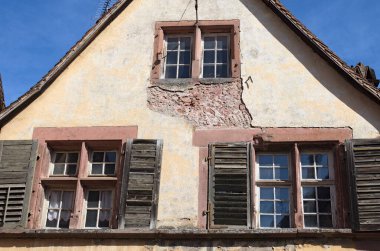 Kiremit çatısının altındaki ortaçağ kaldırımlı ev. Duvarda kırık ahşap panjurları ve soyulmuş boyası olan eski pencereler. Fransa 'nın kuzeydoğusundaki Alsace' de tipik bir mimari. Seyahat ve turizm kavramı.