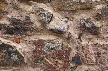 Antik bir el yapımı taş duvarın detaylı görüntüsü. Çok renkli açıkta kalan taş, tuğla ve mineral tabakası. Taş deseni, jeolojik doku. Parlak kırmızı-kahverengi taş arka plan. Soyut arkaplan.