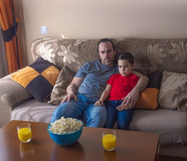 Baba oğul kanepede oturup birlikte televizyon izliyorlar.