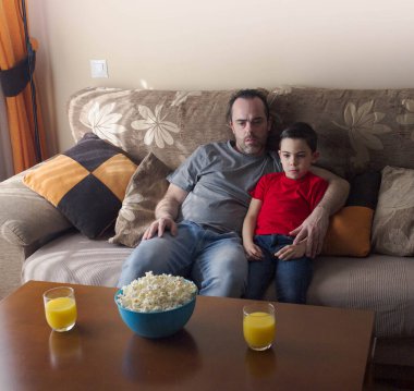 Evde patlamış mısır yiyen bir baba ve oğul. TV izlemek.