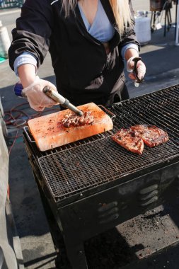 A view of a cook searing a ribeye steak on a Himalayan pink salt block, using a butane torch, seen at a local food festival.