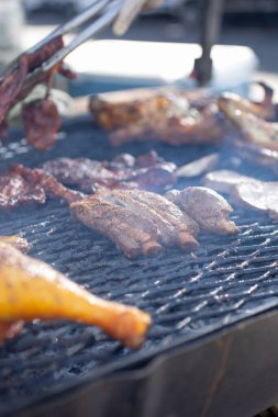 Büyük bir ızgara yüzeyi manzarası, çeşitli et seçimleri içeren Pollo asado ve domuz pirzolası.