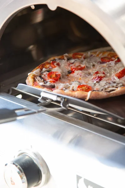 stock image A view of a customized pizza being inserted into a portable pizza oven.