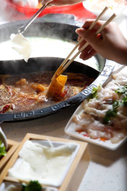 Çiğ eti et kâsesine daldıran bir el sıcak bir restoranın yemeklerinin tüm elementleriyle birlikte görülüyor..