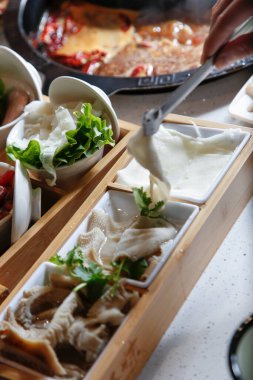 Bir el ve maşa bir dilim çiğ işkembe alıyor, sıcak bir tencere yemeğinin parçası..