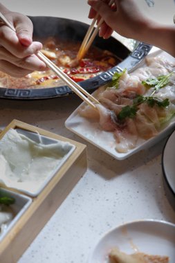 Çiğ eti et kâsesine daldıran bir el sıcak bir restoranın yemeklerinin tüm elementleriyle birlikte görülüyor..