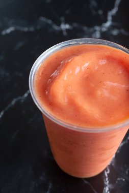Plastik bardaktaki turuncu kırmızı smoothie 'nin yakın çekim görüntüsü.