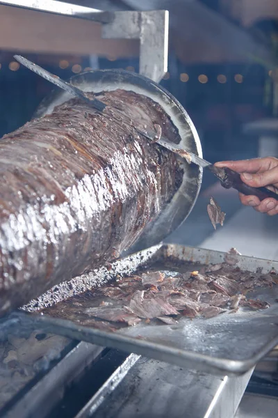 stock image A view of a carving knife cutting trimmings off of beef shawarma cooked on a rotisserie spit.