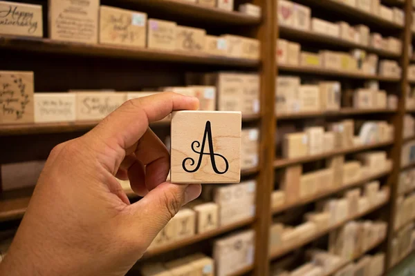 A view of a hand holding the letter A stamp, with a background of stamps on shelves in the background.