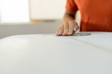 Tamircide sörf tahtasını zımparalayan bir işçinin eli.